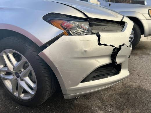 A white Dart with the bumper split open and the headlight hanging